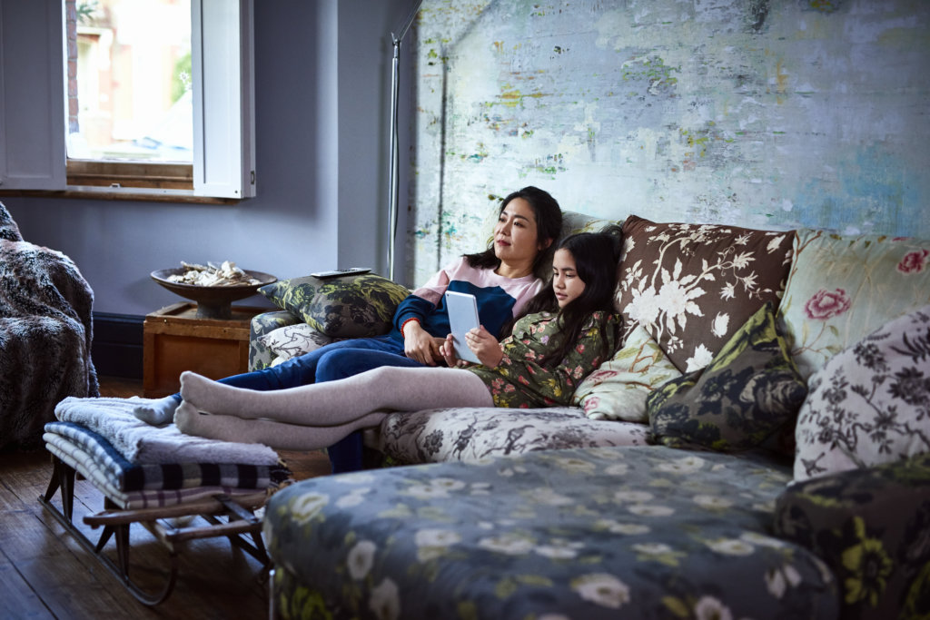 Teenage girl using tablet sitting next to mother on sofa