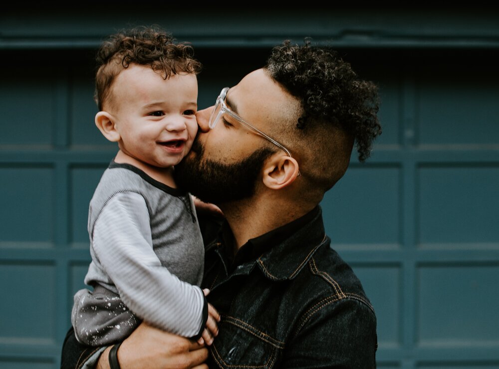 A man kissing a little boy in his arms